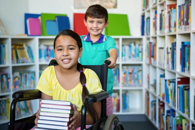 Dos niños exploran una biblioteca; una de ellos usa una silla de ruedas.